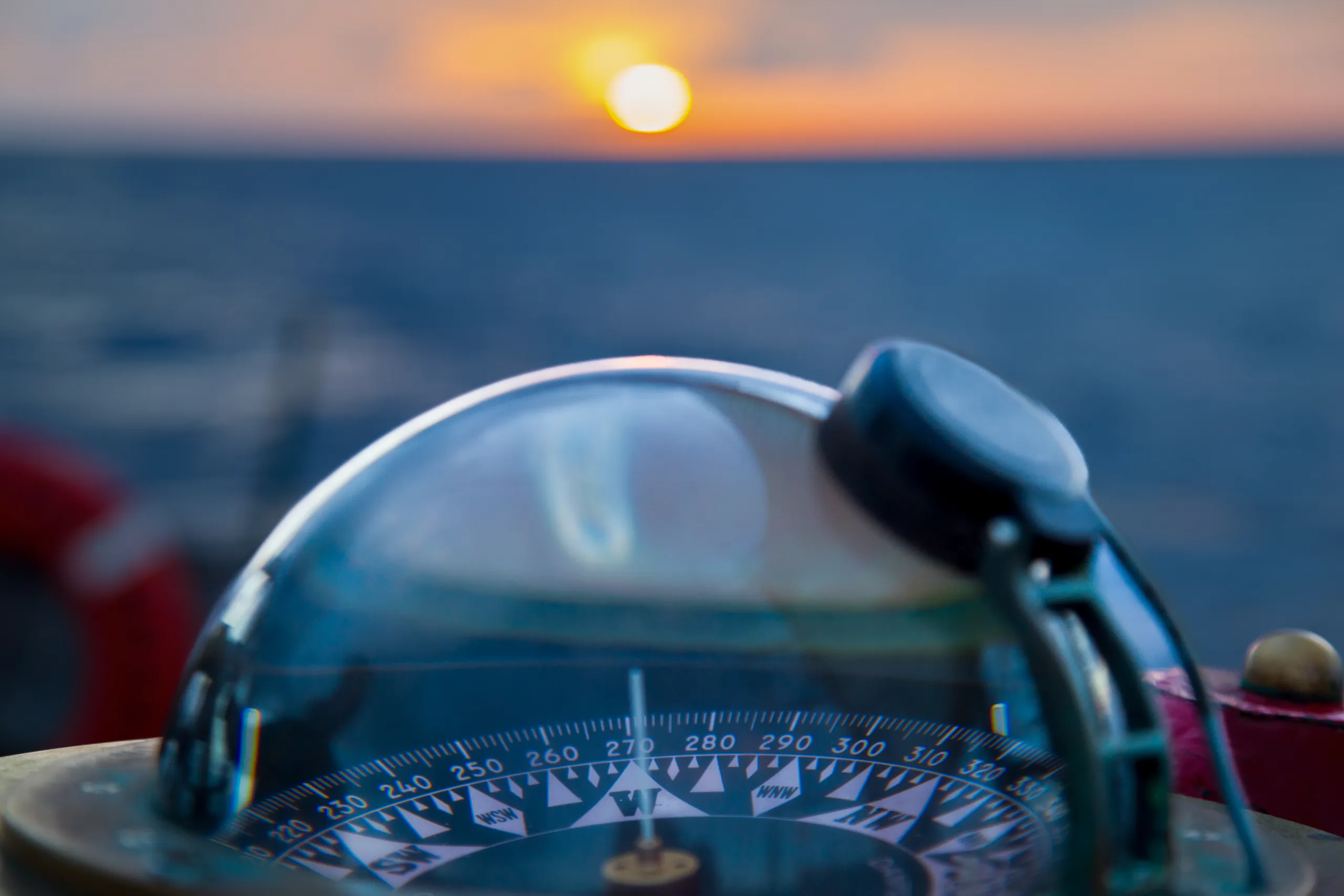 closeup view of boat's compass pointing west into sunset over ocean